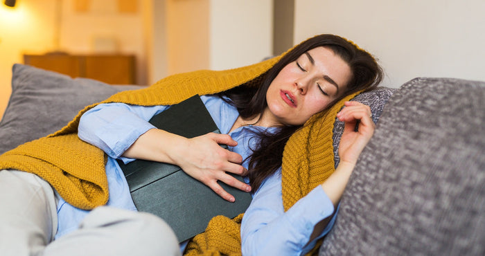 Eine junge Frau ist beim lesen auf ihrem Sofa eingeschlafen.