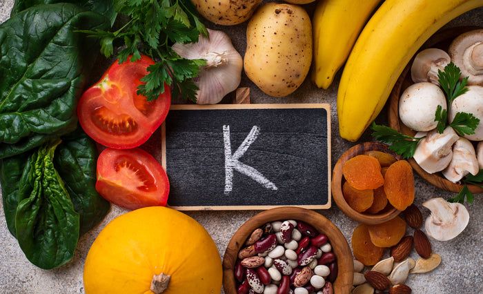 Kaliumreiche Lebensmittel liegen verteilt um ein Schild mit der Aufschrift K, auf einer Tischplatte verteilt.