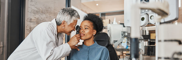 Eine Frau sitzt beim Ophthalmologe, welcher Ihre Augen untersucht.