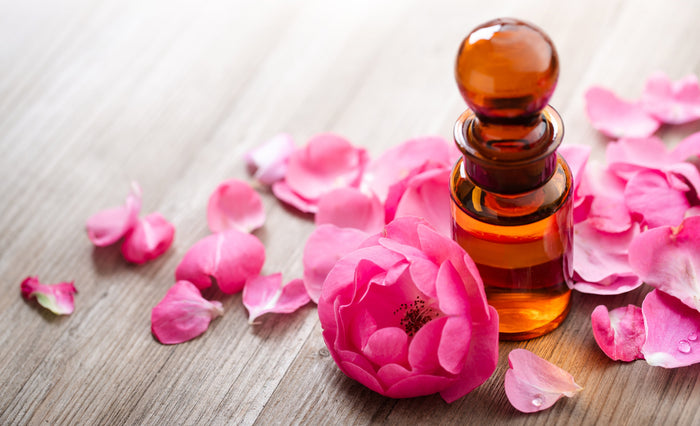 Auf einem Holztisch steht ein Fläschen gefüllt mit ätherischen Öl und daneben liegt eine Rosenblüte.