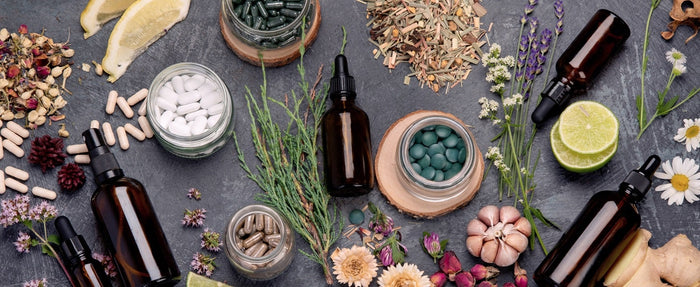 Verschiedene Öle, Nahrungsergänzungsmittel und Pflanzen liegen auf einer schwarzen Granittischplatte.