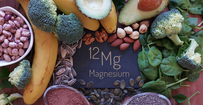 Magnesiumreiche Lebensmittel liegen verteil auf einem Tisch. In der Mitte liegt eine Tafel mit der Aufschrift Magnesium.